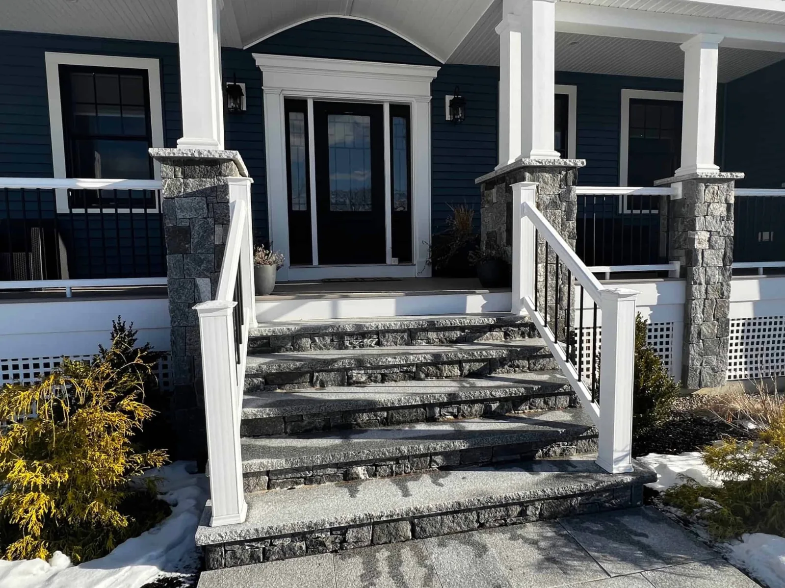 Front entry steps with stone-faced risers and stone-clad porch columns bordered by white railings