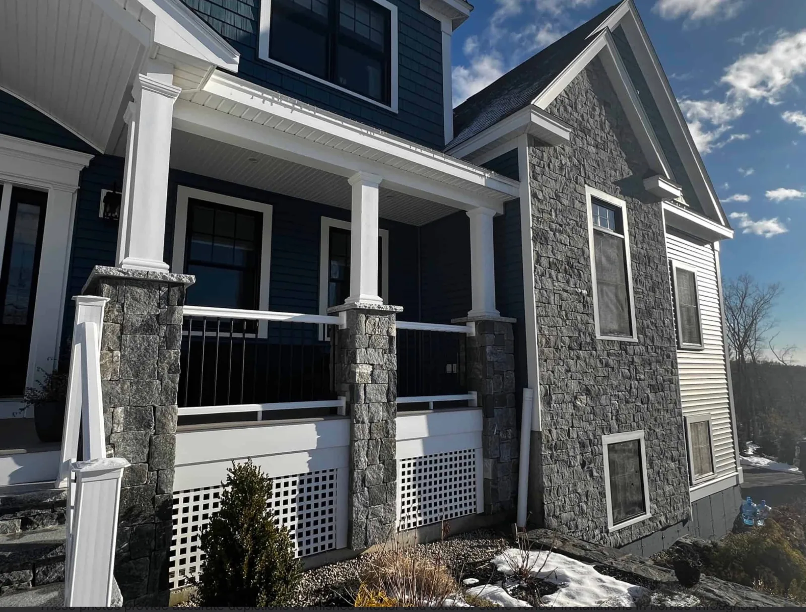 Gray stone veneer on a house facade and porch column bases with white trim and dark siding