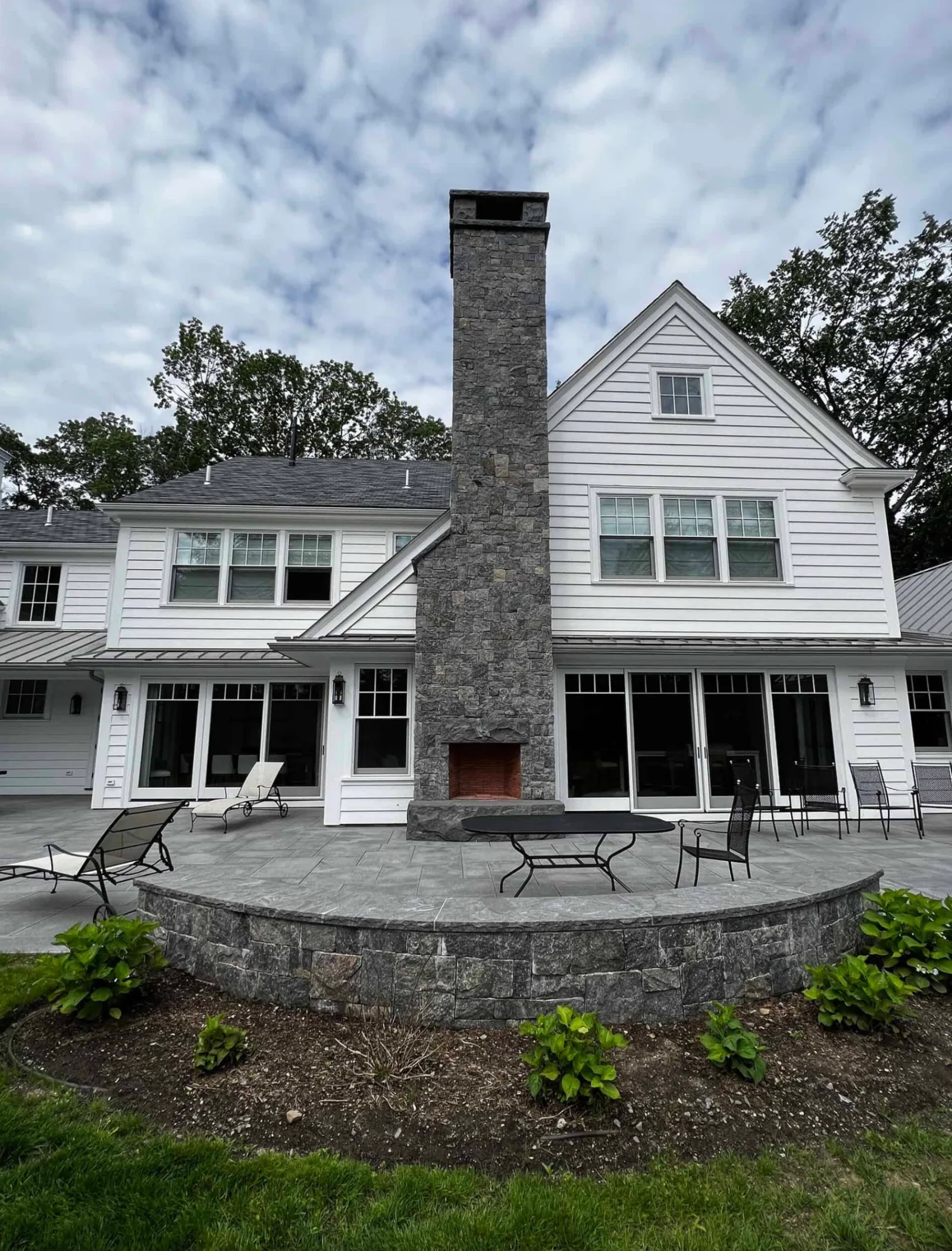 Tall stone-clad chimney with an outdoor fireplace overlooking a patio and curved stone wall